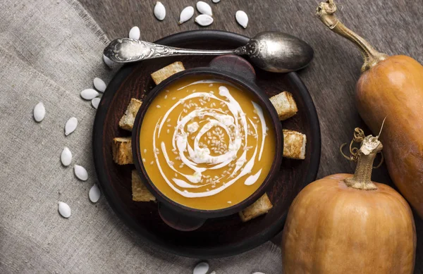 Soupe de citrouille avec crème et graines de sésame dans un bol en céramique marron sur fond en bois. Couché plat, vue du dessus. — Photo