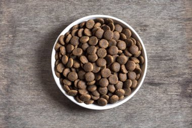 Ahşap arka planda beyaz bir seramik kasede kurutulmuş hayvan yiyeceği.