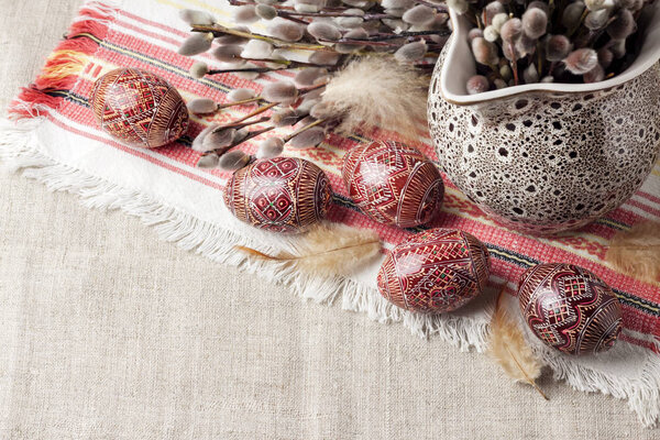 Easter still life with Pysanka and willow branches in ceramic jug on traditional Ukrainian cloth. Decorated Easter eggs, traditional for Eastern Europe culture. Copy space