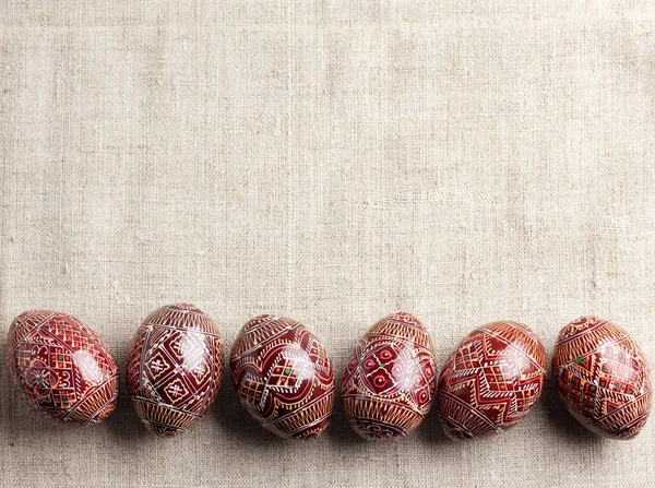 Традиционная украинская пысанка выстроилась в линию на льняном фоне. Украшенные пасхальные яйца, традиционные для культуры Восточной Европы. Плоская кладка, вид сверху, копировальное пространство — стоковое фото