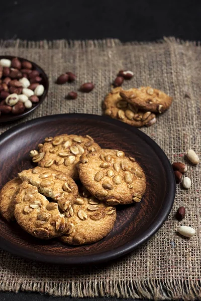 Biscuits aux arachides faits maison sur une assiette brune avec des arachides crues en arrière-plan. Cuisine de style rustique — Photo