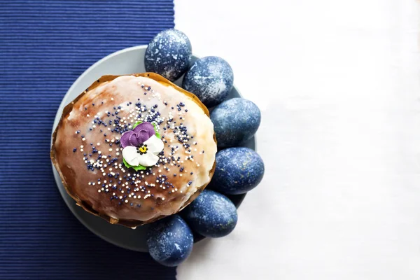 Gâteau de Pâques décoré de fleurs de sucre et d'œufs de couleur bleue sur une assiette sur fond de tissu blanc et bleu avec espace de copie. Les œufs étaient colorés en bleu avec une décoction d'hibiscus. Couché plat, vue du dessus — Photo