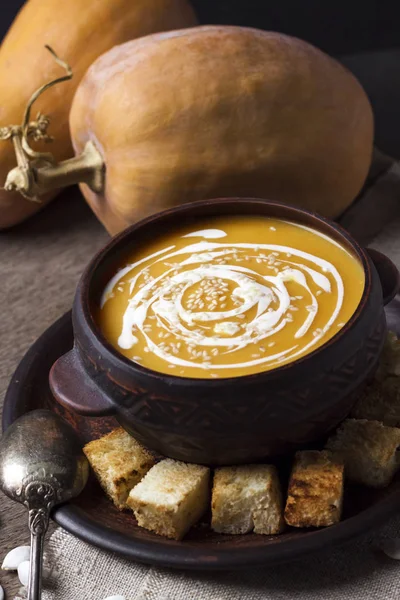 Гарбузовий суп з вершками та насінням кунжуту в коричневій керамічній мисці на дерев'яному фоні — стокове фото