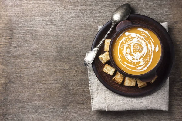 Soupe de citrouille avec crème et graines de sésame dans un bol en céramique marron sur fond en bois. Couché plat, vue du dessus. — Photo