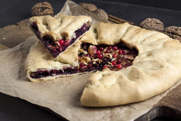Homemade galette pie with apples, elder berries and walnuts decorated with fresh cowberry on rustic dark background
