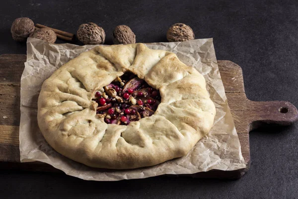 Homemade galette pie with apples, elder berries and walnuts decorated with fresh cowberry on rustic dark background