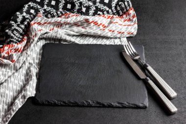 Siyah arka planda çatal, bıçak ve masa örtüsü olan siyah bir levha. Masa ayarı. Düz konum, üst görünüm, kopyalama alanı