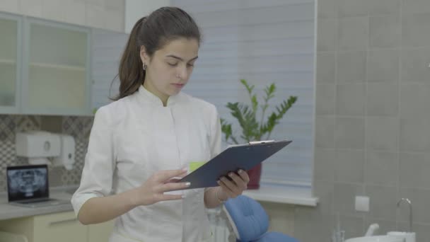 Молодая привлекательная женщина-врач проверяет медицинскую карту пациента . — стоковое видео