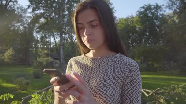 Mujer joven atractiva usando su teléfono de pantalla táctil en el parque 4K — Vídeos de Stock