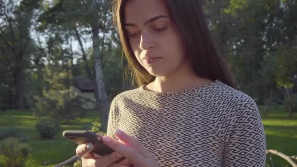 Attrayant jeune femme en utilisant son téléphone à écran tactile dans le parc 4K — Video