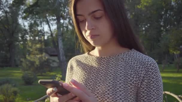 Attraktive junge Frau mit ihrem Touchscreen-Handy im Park 4k — Stockvideo