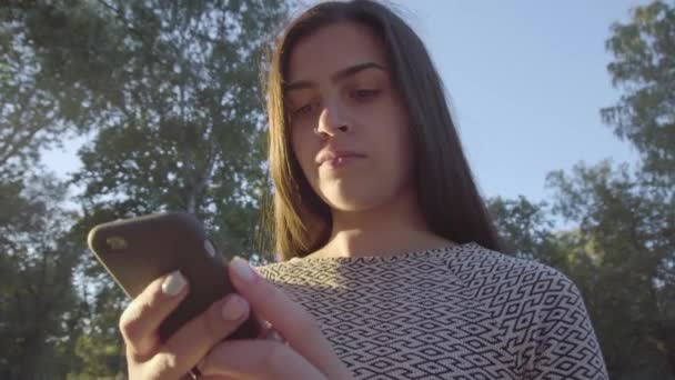 Привлекательная молодая женщина с сенсорным экраном телефона в парке 4K — стоковое видео