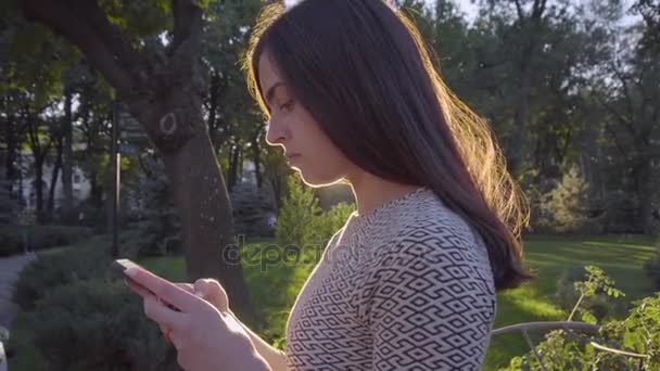Привлекательная молодая женщина с сенсорным экраном телефона в парке 4K — стоковое видео
