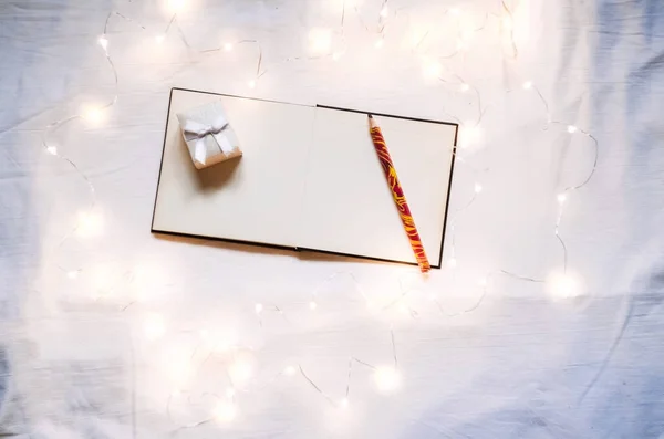 good New Year spirit. blank notebook for entries of desires and goals for the new year. garlands shine. view from above. background white