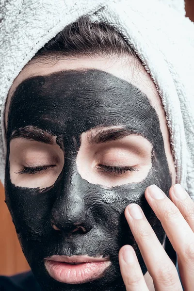 the girl applies a clay face mask with her eyes closed.
