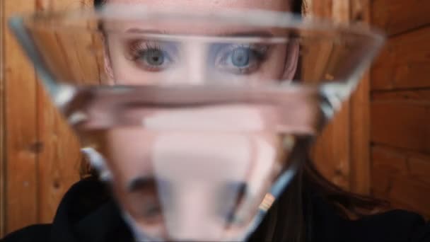 Close-up. beautiful girl plays with a glass of water. distortion. beautiful eyes. facial expressions. crooked at the camera. — Stock Video