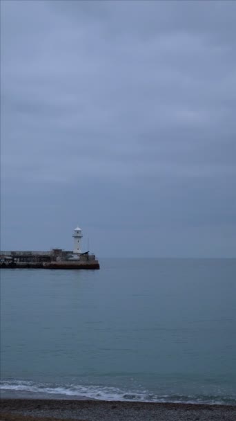 phare. Le phare côtier est éclairé en rouge. ciel nuageux, vagues de mer. vidéo verticale 