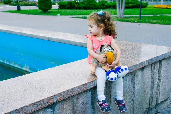 Pequena menina sentada no parque com brinquedo — Fotografia de Stock