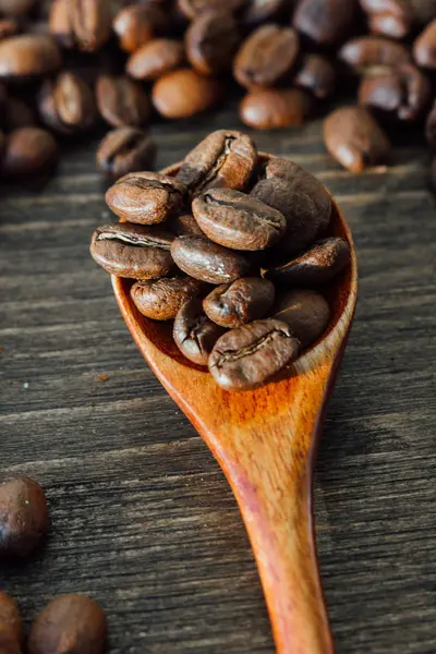 Vista superior de la cucharadita de madera llena de granos de café redondeados con semillas de café sobre el fondo de madera — Foto de Stock