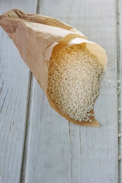 Семена белого кунжута на бумажном корнете над белым столом — стоковое фото