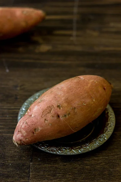 Ahşap masa üzerinde metal plaka üzerindeki ham tatlı patates.