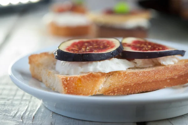 Bruschetta com queijo de cabra e figos em prato branco — Fotografia de Stock