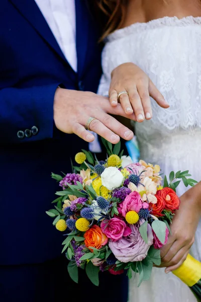 Bruid en bruidegom demonstreren ringen op hun handen tegen bloemboeket als achtergrond. — Stockfoto