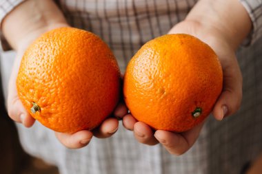 Elinde olgun iki portakal tutan bir kadın..