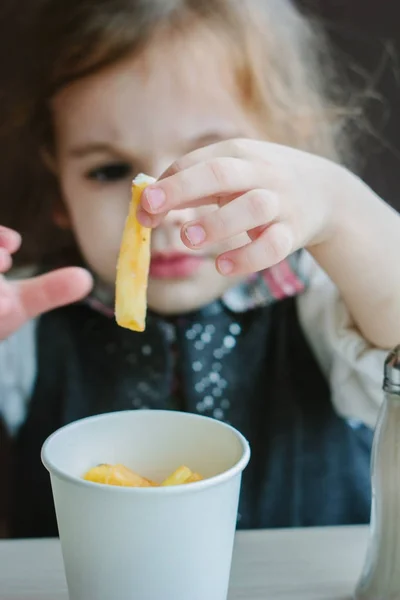 Маленькая девочка ест картошку фри в ресторане. — стоковое фото
