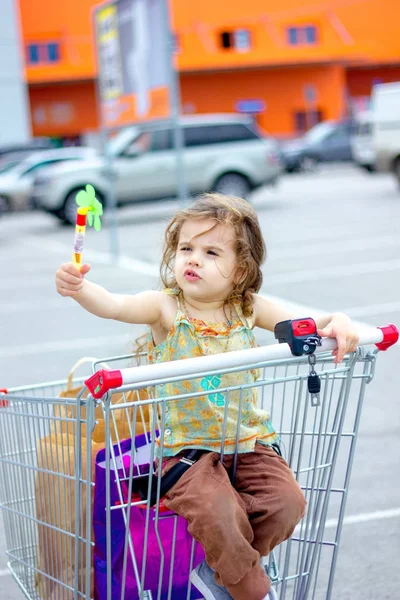Niña divirtiéndose sentada en un carrito de compras cerca del centro comercial . — Foto de Stock