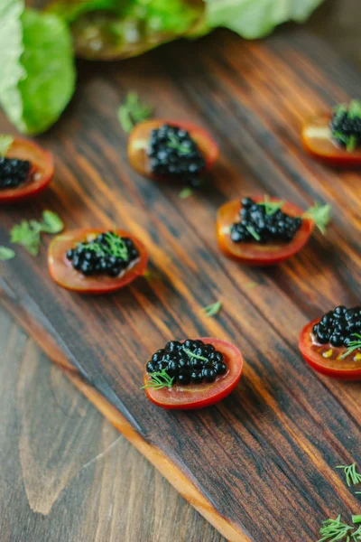 Tomates cereja vermelhos e aperitivos de caviar preto em tábua de madeira . — Fotografia de Stock