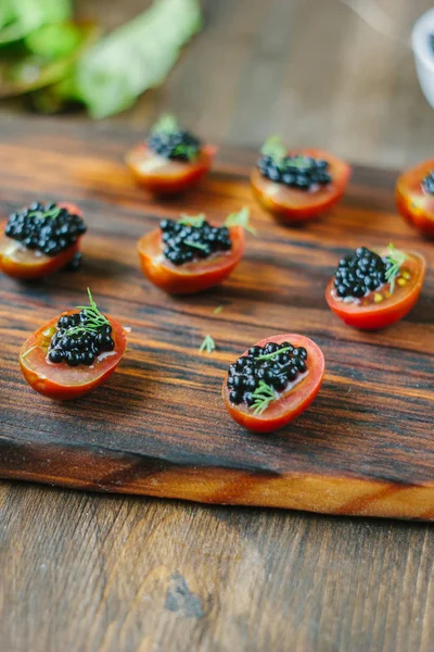 Pequenos aperitivos com tomate cereja e caviar preto . — Fotografia de Stock