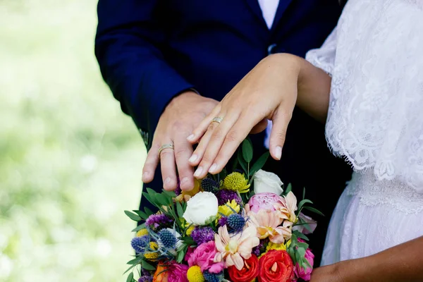 Bride and groom demonstrating rings on their hands against flower bouquet as background. — Stock Photo, Image