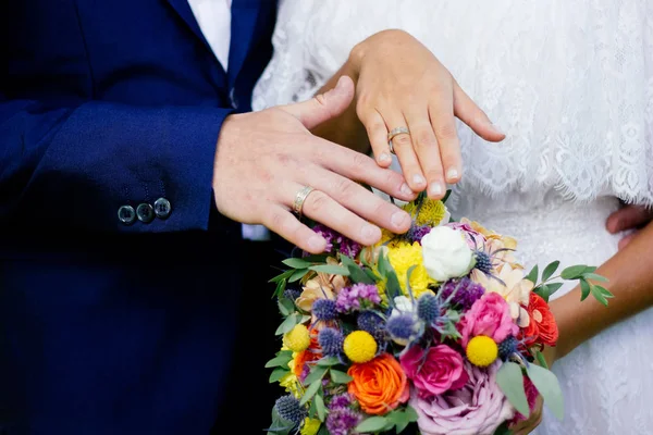 Novia y novio demostrando anillos en sus manos contra ramo de flores como fondo . — Foto de Stock