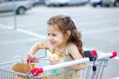 Alışveriş arabasının park yerinde donut yerken gülümseyen küçük kız..
