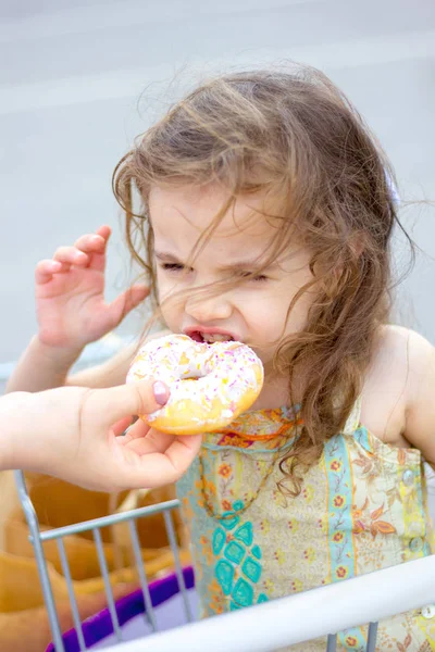 Adorable chica comiendo donut en el aparcamiento del centro comercial después de ir de compras . — Foto de Stock