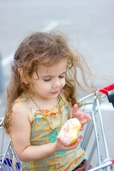 Adorable chica comiendo donut en el aparcamiento del centro comercial después de ir de compras . — Foto de Stock