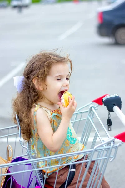 Маленькая девочка сидит за тележкой и ест пончики . — стоковое фото