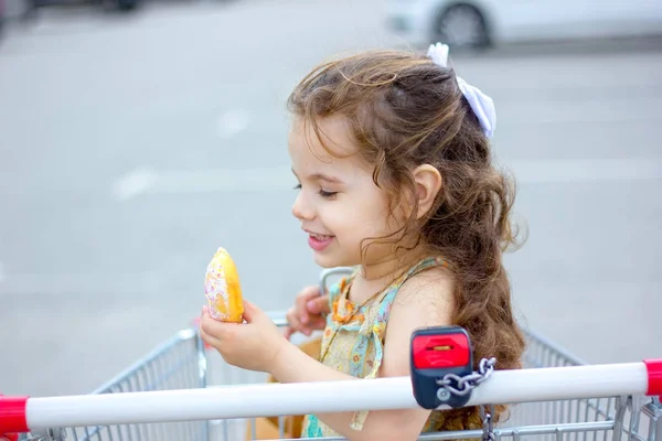 Niña comiendo una dona en el estacionamiento del centro comercial . — Foto de Stock