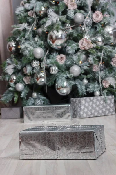 Un regalo in carta argentata sul pavimento con l'albero di Natale sullo sfondo . — Foto Stock