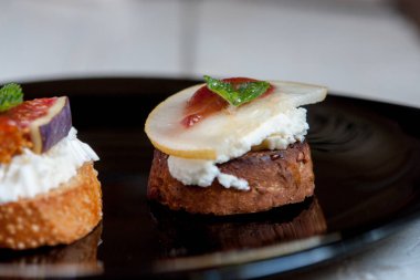 Bruschetta keçi peyniri, armut ve incir siyah plaka üzerinde