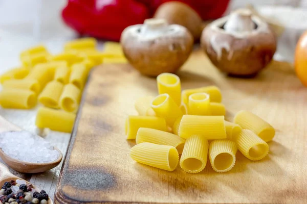 Pasta seca de rigatoni sobre tabla de cocina de madera con verduras. —  Fotos de Stock