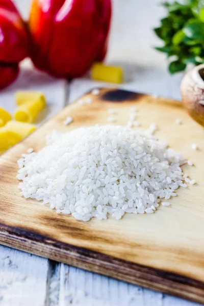 Arroz blanco seco sobre el tablero de la cocina con algunas verduras y pasta alrededor . — Foto de Stock