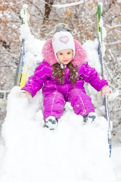 Kid girl on children slide at snowy winter day. — Stock Photo, Image