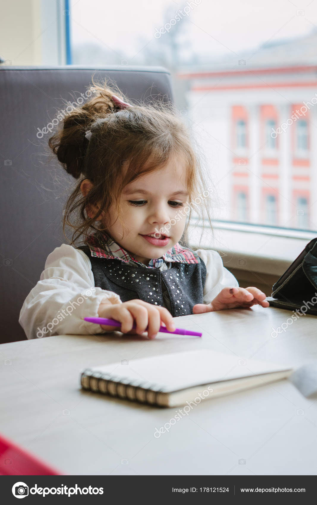 Little kid girl writing or drawing with pen in scetch book ...