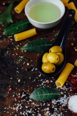 Diğer malzemelerle çevrili siyah kaşıkta zeytinler.
