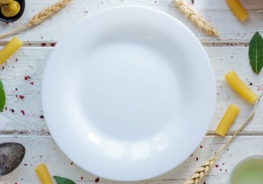 İtalyan tortiglioni makarna, defne yaprağı ve diğer maddeler çevrili beyaz seramik tabak.