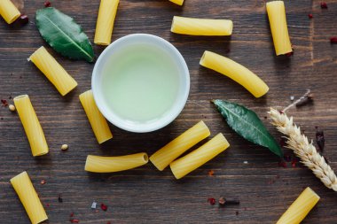 Koyu yapraklı Tortiglioni makarnası, zeytinyağı ve kahverengi ahşap yüzeydeki diğer malzemeler..