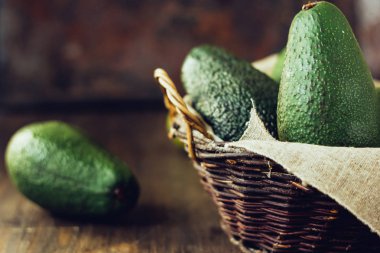 Ahşap arka planda Avokado meyveleri sepette.