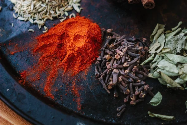 Set of spices - chili powder, cloves, curry leaves and caraway over black surface. — Stock Photo, Image